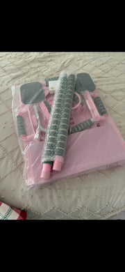 A pink and gray hair styling tool set inside a clear plastic bag, placed on a white quilted bedspread.