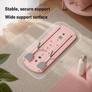 A pink adjustable support pad or tray with gray foot-like pads and white handles, shown on a beige rug in a styled indoor setting with overlaid text reading 'Stable, secure support' and 'Wide support surface.'.
